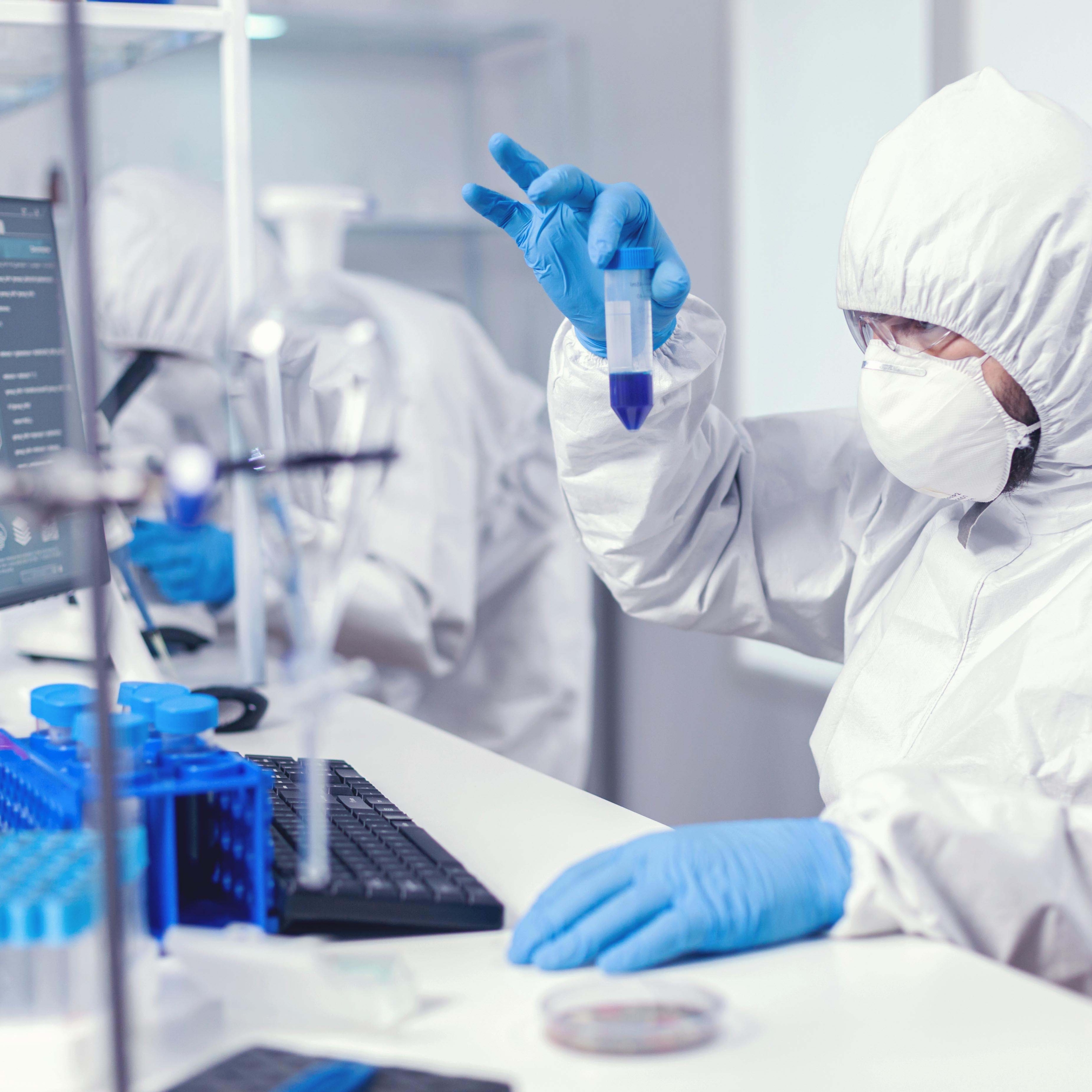 Scientist in lab coversall looking closely at sample in test tube